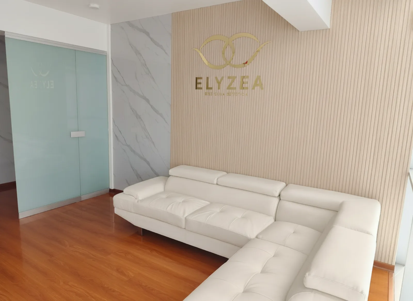 Recepción de Elyzea en Miraflores con logo dorado en pared de madera y sofá blanco de cuero